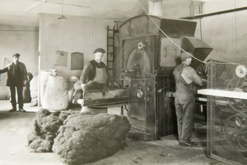 A black and white indoor shot depicts several workers operating machinery in the Glencraft mattress making factory.