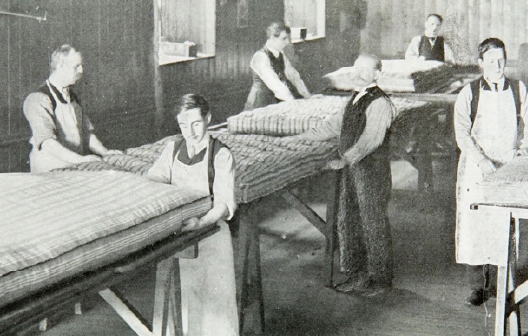 A black and white indoor shot depicts several workers operating machinery in the Glencraft mattress making factory.